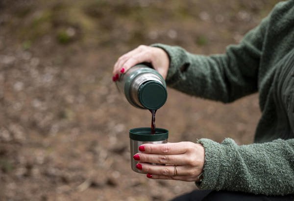 Detaljbild på kvinna som häller upp kaffe ur en termos i skogen