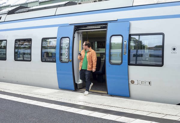 Man i orange jacka går av pendeln och håller i telefonen
