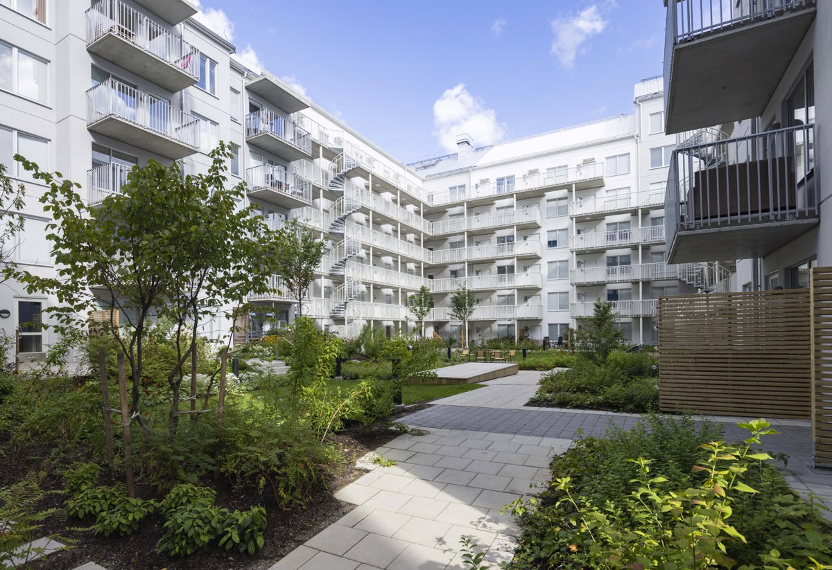 Grönskande innergård inringad av vita flerfamiljshus.