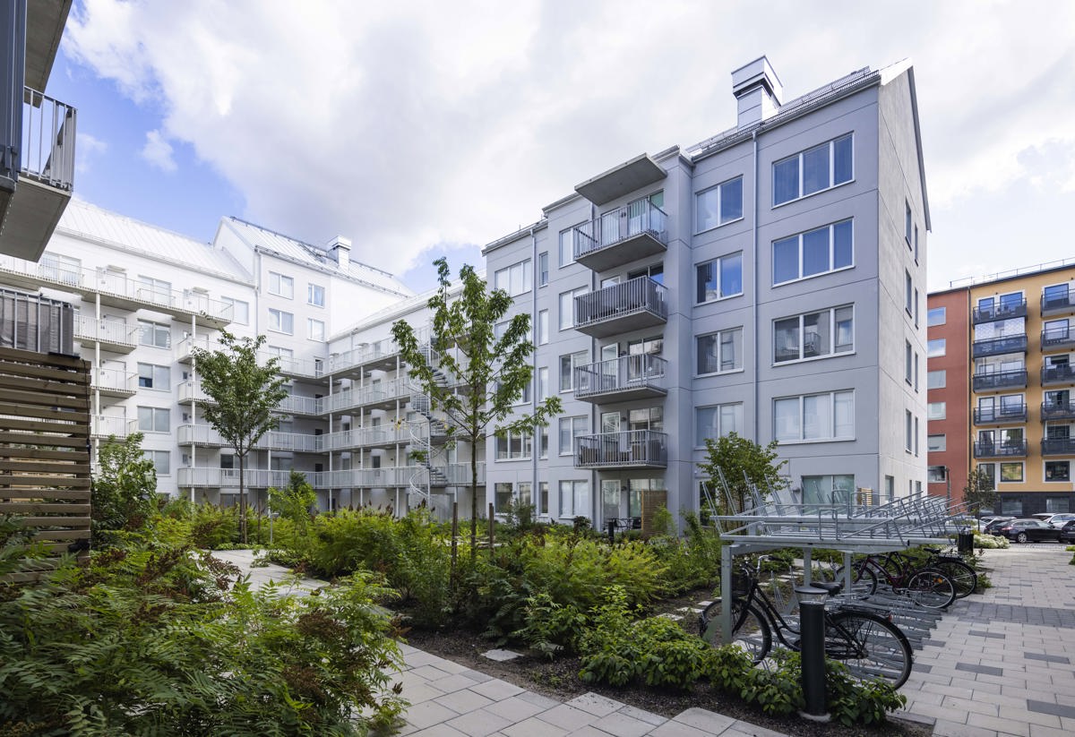 Grönskande innergård inringat av ett vitt flerfamiljshus.